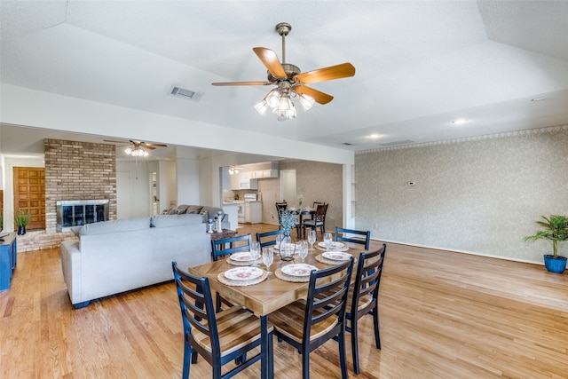 dining area with ceiling fan, a fireplace, a textured ceiling, and light wood-type flooring