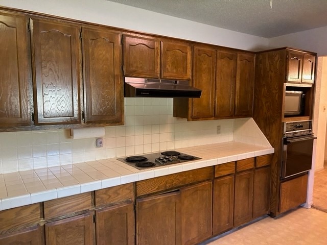 kitchen featuring a textured ceiling, tile countertops, white electric cooktop, decorative backsplash, and black oven