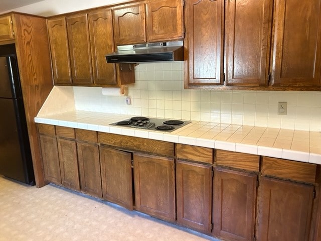 kitchen with electric stovetop, black refrigerator, decorative backsplash, and tile countertops