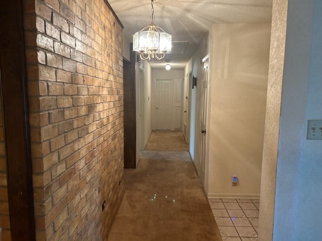 corridor with light tile patterned floors, a notable chandelier, and brick wall