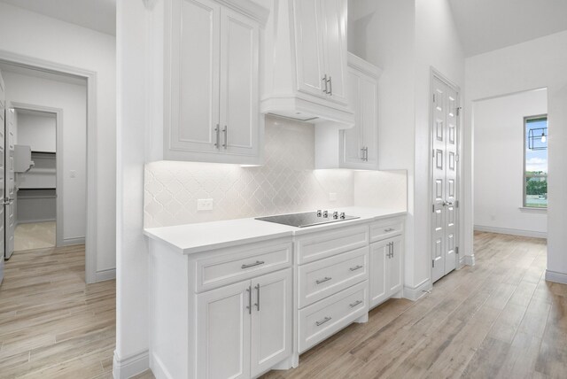 kitchen with light countertops, backsplash, white cabinetry, light wood-type flooring, and black electric cooktop