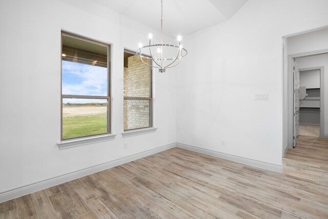 empty room with baseboards, a chandelier, and light wood-style floors