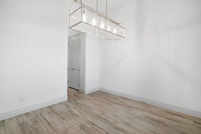 spacious closet with light wood finished floors and an inviting chandelier