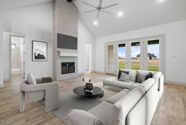 living room with light hardwood / wood-style flooring, high vaulted ceiling, ceiling fan, and a stone fireplace