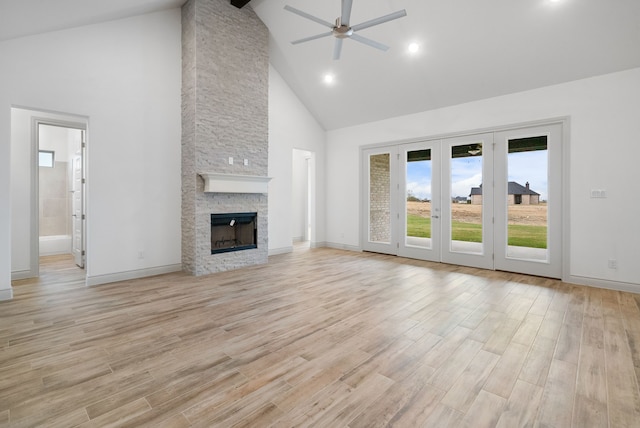 unfurnished living room featuring light wood-style floors, high vaulted ceiling, a ceiling fan, and a stone fireplace