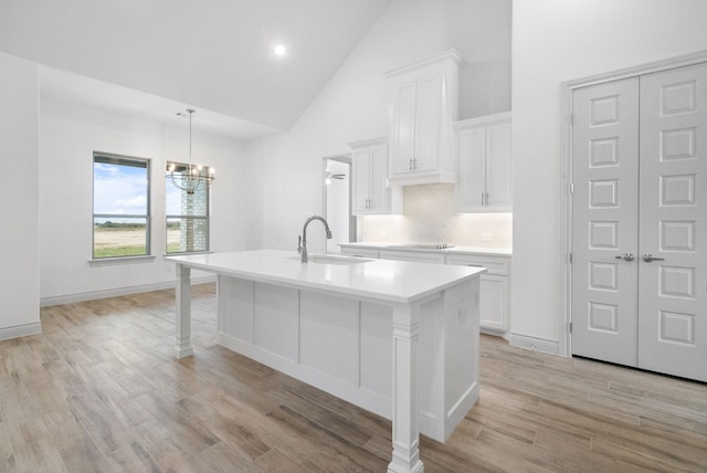 kitchen with a center island with sink, white cabinets, light countertops, light wood-type flooring, and a sink