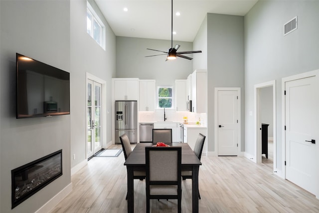 dining area with sink, light wood-type flooring, ceiling fan, and a high ceiling