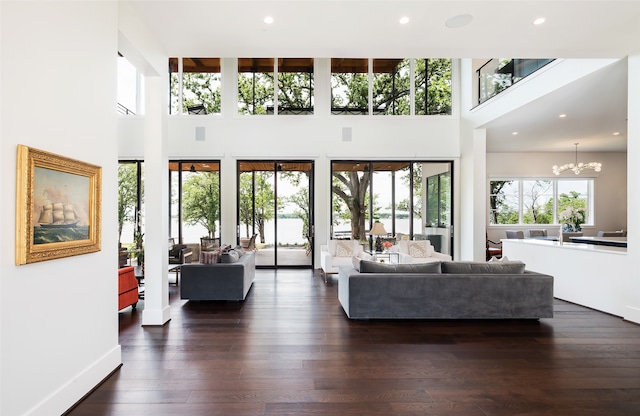 living room featuring a healthy amount of sunlight, a high ceiling, a notable chandelier, and dark hardwood / wood-style flooring