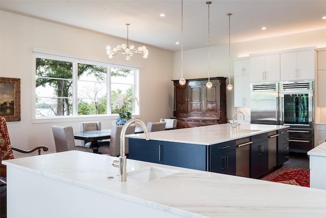 kitchen with decorative light fixtures, a kitchen island with sink, sink, and white cabinets