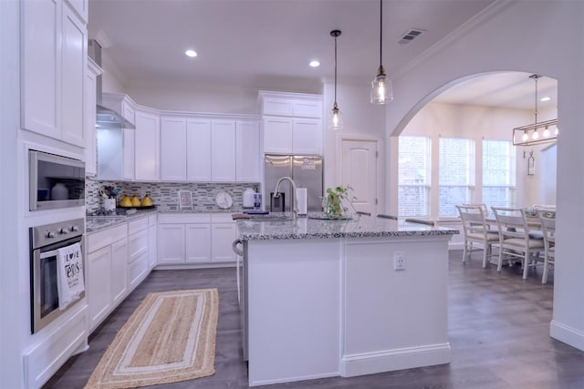 kitchen with white cabinets, hanging light fixtures, an island with sink, light stone counters, and stainless steel appliances