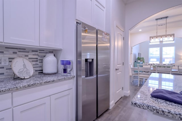 kitchen featuring white cabinets, stainless steel refrigerator with ice dispenser, tasteful backsplash, and pendant lighting