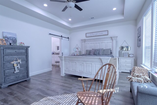 bedroom with a barn door, dark wood-type flooring, a tray ceiling, and multiple windows