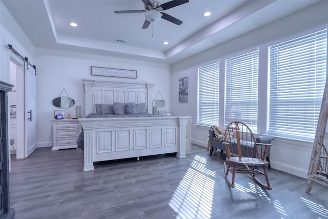 bedroom with a raised ceiling, a barn door, ceiling fan, and dark hardwood / wood-style flooring