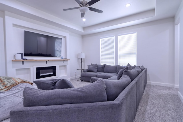 carpeted living room with a raised ceiling and ceiling fan