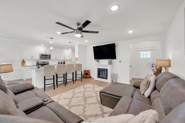 living room with light wood-style floors, recessed lighting, a glass covered fireplace, and ceiling fan