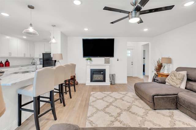 living area featuring a glass covered fireplace, baseboards, recessed lighting, a ceiling fan, and light wood finished floors