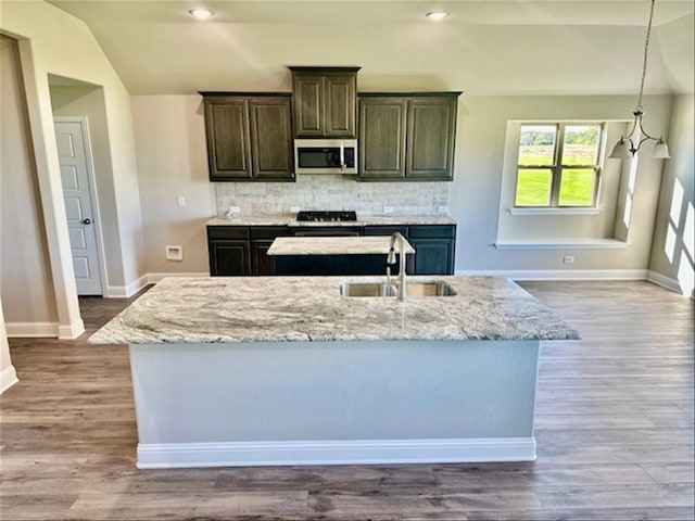 kitchen with tasteful backsplash, sink, hardwood / wood-style floors, and a center island with sink