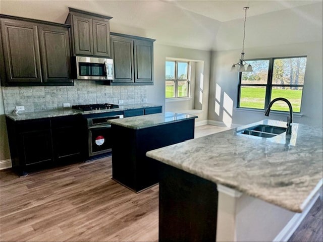 kitchen with sink, a healthy amount of sunlight, light stone counters, a kitchen island with sink, and black appliances