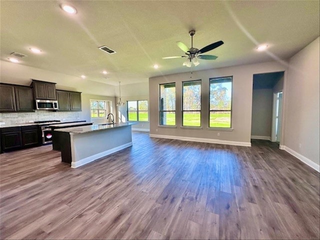 kitchen featuring decorative backsplash, stainless steel appliances, ceiling fan, hardwood / wood-style flooring, and a center island with sink