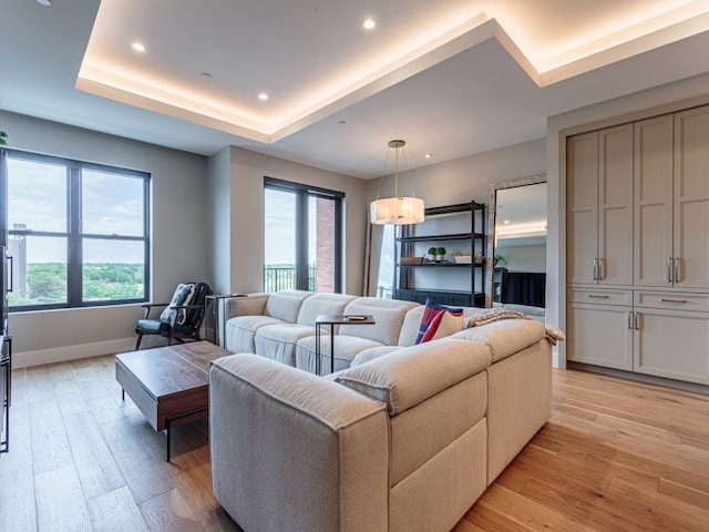 living room featuring plenty of natural light, light hardwood / wood-style flooring, and a raised ceiling