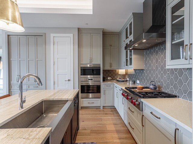 kitchen featuring appliances with stainless steel finishes, tasteful backsplash, sink, wall chimney range hood, and light wood-type flooring