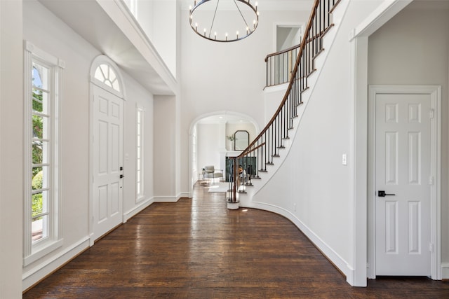 entrance foyer featuring dark wood-type flooring, plenty of natural light, a chandelier, and a towering ceiling