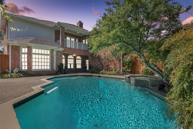 pool at dusk featuring an in ground hot tub