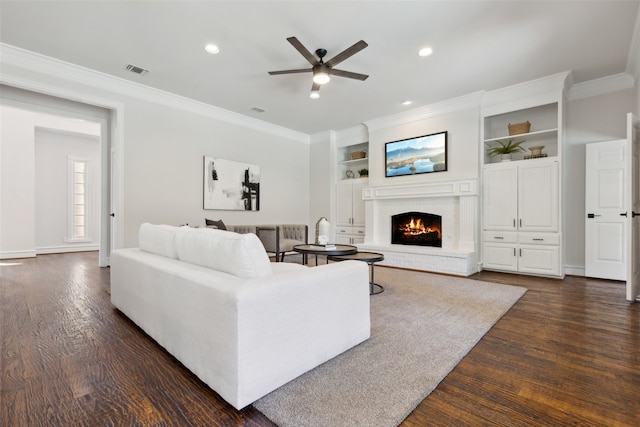 living room with dark wood-type flooring, ceiling fan, ornamental molding, and a fireplace