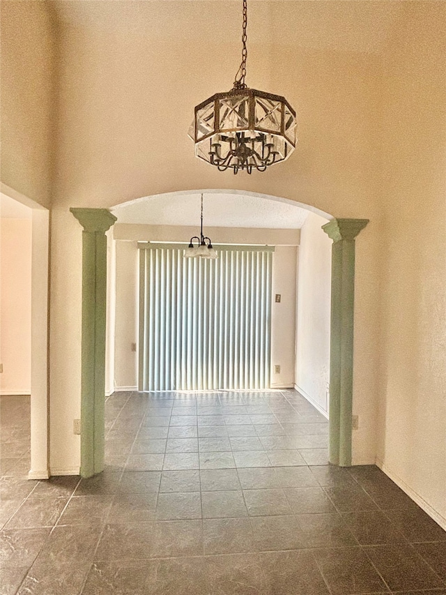 unfurnished room featuring an inviting chandelier, a high ceiling, and decorative columns