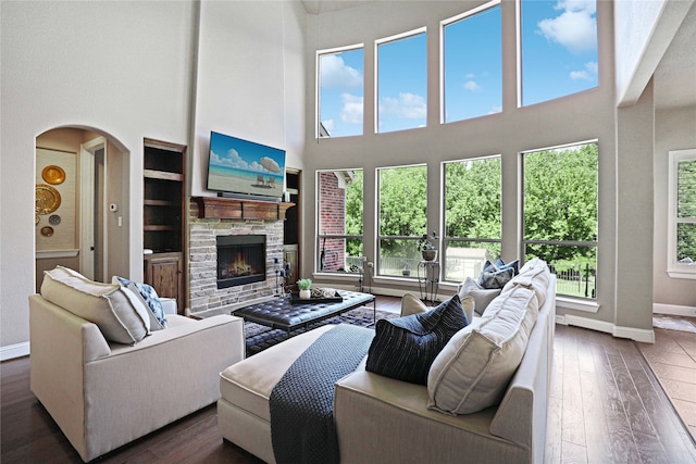 living room with built in shelves, a fireplace, dark wood-type flooring, and a high ceiling