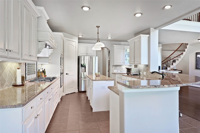 kitchen with a center island, appliances with stainless steel finishes, white cabinetry, light stone counters, and kitchen peninsula