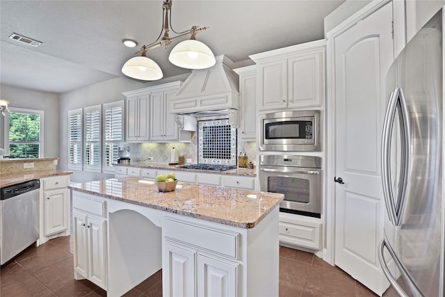 kitchen with white cabinets, decorative light fixtures, stainless steel appliances, and a kitchen island