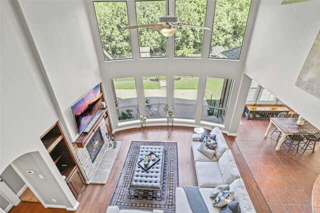 living room featuring a tile fireplace, ceiling fan, a high ceiling, and hardwood / wood-style flooring