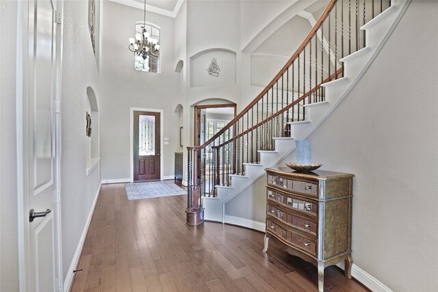 foyer entrance featuring hardwood / wood-style floors, a high ceiling, ornamental molding, and a notable chandelier