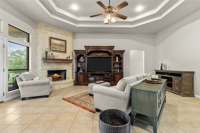 tiled living room with a textured ceiling, a raised ceiling, ceiling fan, and a fireplace