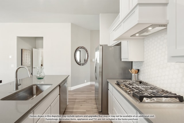 kitchen featuring white cabinets, light wood-type flooring, appliances with stainless steel finishes, sink, and premium range hood