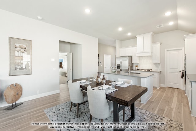 dining space with sink, light hardwood / wood-style floors, and vaulted ceiling