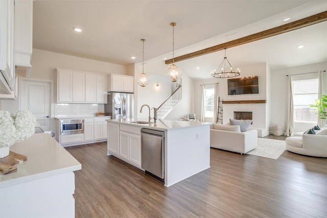 kitchen featuring beamed ceiling, appliances with stainless steel finishes, white cabinetry, and a kitchen island with sink