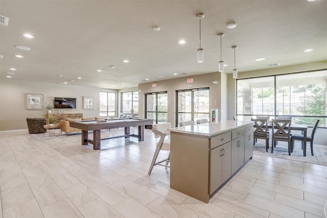 kitchen with light stone counters, gray cabinetry, a kitchen island, hanging light fixtures, and pool table