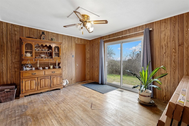 interior space with light wood-style floors, visible vents, wood walls, and ceiling fan