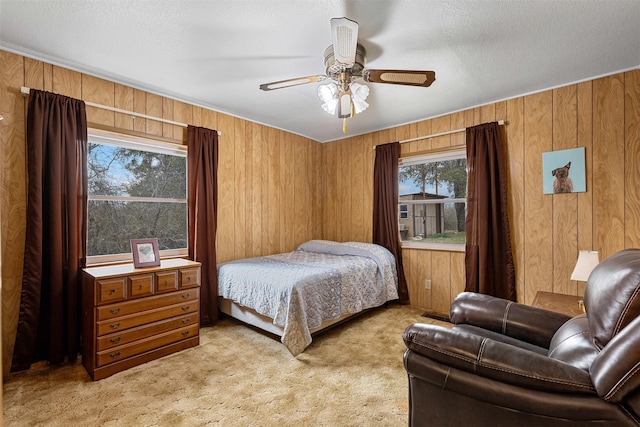 bedroom featuring light colored carpet, ceiling fan, wooden walls, and a textured ceiling