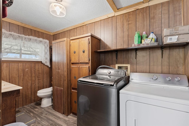 clothes washing area with washer and clothes dryer, wood walls, a textured ceiling, wood finished floors, and laundry area