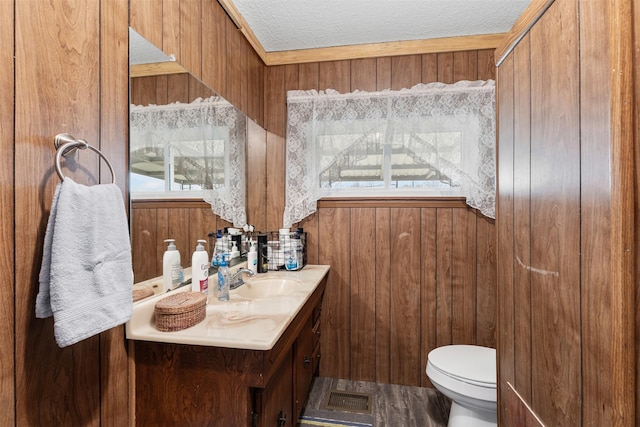 half bath with toilet, wooden walls, a textured ceiling, and vanity