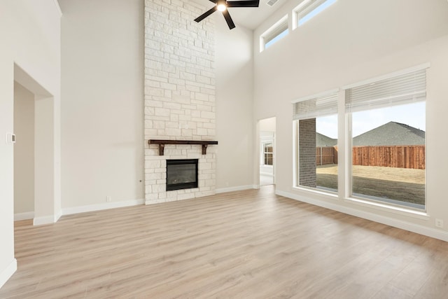 unfurnished living room featuring light wood-type flooring, ceiling fan, a stone fireplace, and a towering ceiling