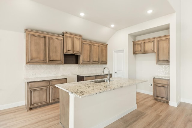 kitchen featuring an island with sink, sink, tasteful backsplash, and light stone counters