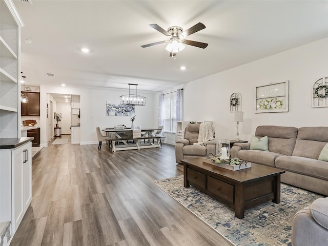 living room with ceiling fan with notable chandelier and hardwood / wood-style flooring