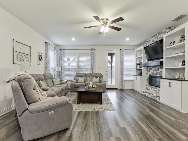 living room with dark hardwood / wood-style floors, ceiling fan, and a stone fireplace