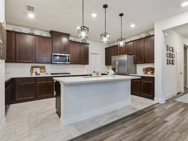 kitchen with a center island with sink, pendant lighting, appliances with stainless steel finishes, sink, and dark brown cabinetry