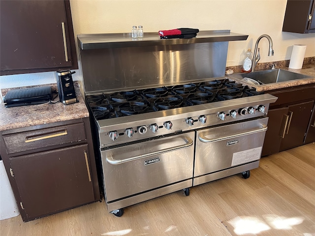 kitchen with high end range, sink, dark brown cabinets, and light hardwood / wood-style flooring