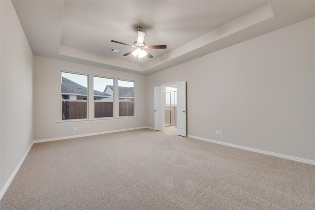 carpeted spare room featuring a tray ceiling and ceiling fan